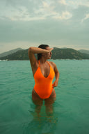 Femme portant le maillot de bain une pièce Ama orange dans une eau claire et verte