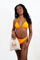 Femme portant le haut de maillot de bain Sasha orange, le bas de maillot de bain Hena en orange et le pochon LNI swimwear orange également